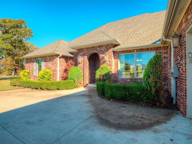 doorway to property with brick siding and roof with shingles