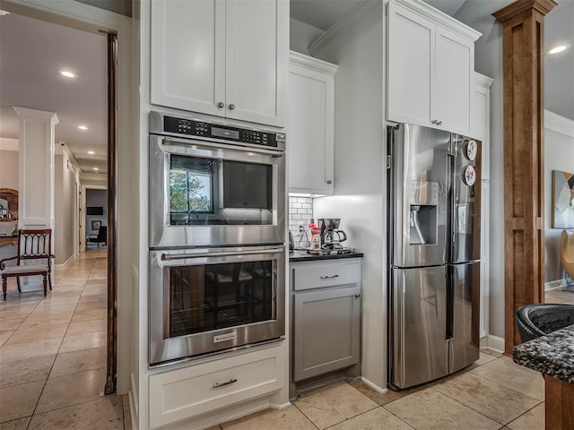 kitchen with dark countertops, backsplash, decorative columns, appliances with stainless steel finishes, and white cabinets