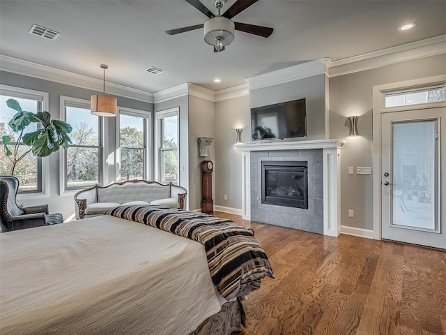 bedroom with wood finished floors, visible vents, baseboards, a fireplace, and ornamental molding