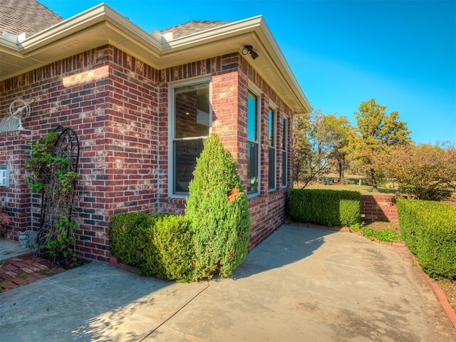 view of home's exterior with a patio area, brick siding, and a shingled roof