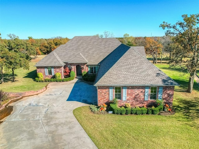 view of front of house with brick siding, a front lawn, driveway, and a shingled roof