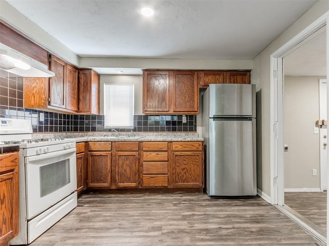 kitchen featuring tasteful backsplash, white gas stove, light countertops, freestanding refrigerator, and light wood-style floors