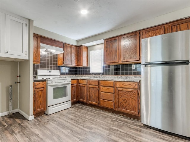 kitchen with light wood-type flooring, freestanding refrigerator, decorative backsplash, under cabinet range hood, and white gas range