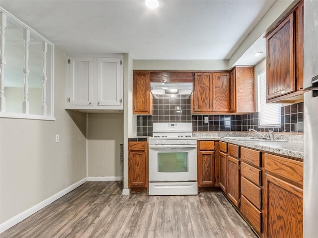 kitchen featuring backsplash, extractor fan, light wood-type flooring, white gas range oven, and a sink