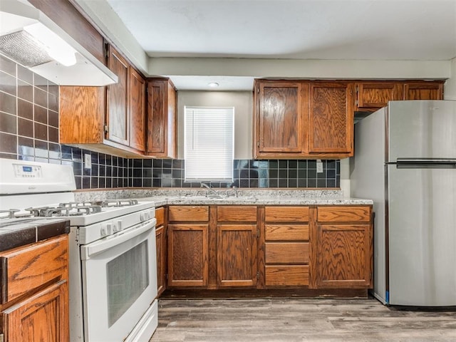 kitchen featuring light wood-style flooring, custom range hood, backsplash, freestanding refrigerator, and white gas range