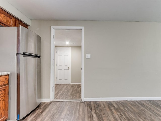 kitchen with brown cabinetry, wood finished floors, baseboards, and freestanding refrigerator