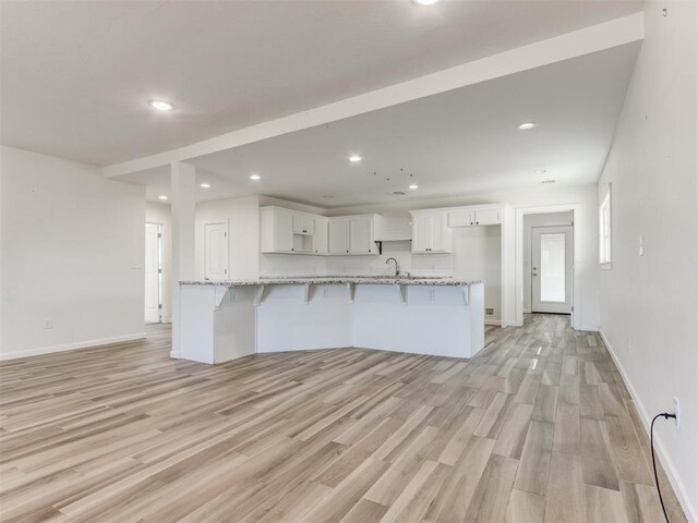 kitchen with white cabinets, light wood-style floors, a kitchen breakfast bar, and a sink