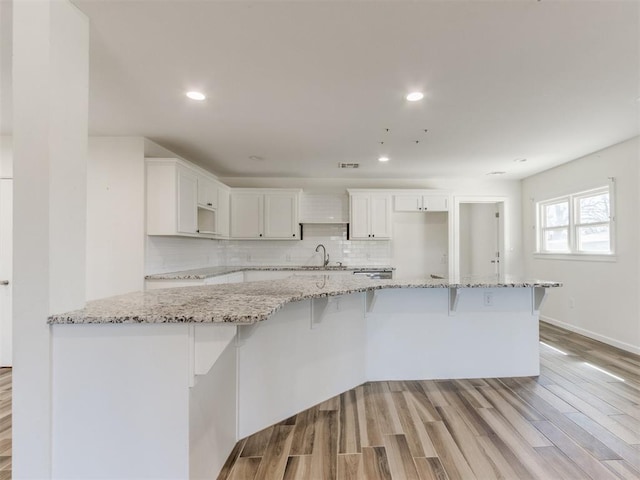 kitchen with tasteful backsplash, white cabinets, light wood-style floors, and a kitchen breakfast bar