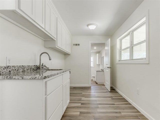 kitchen with baseboards, visible vents, white cabinets, light wood-type flooring, and a sink