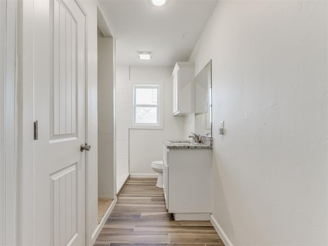 bathroom with toilet, baseboards, wood finished floors, and vanity