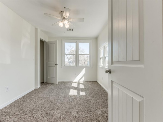 carpeted empty room featuring ceiling fan, visible vents, and baseboards