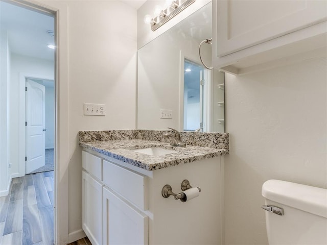 half bathroom with toilet, baseboards, wood finished floors, and vanity