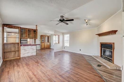 unfurnished living room with baseboards, lofted ceiling, ceiling fan with notable chandelier, wood finished floors, and a glass covered fireplace