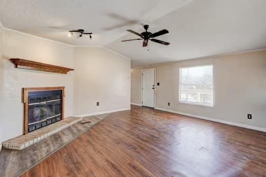 unfurnished living room with wood finished floors, baseboards, lofted ceiling, ceiling fan, and a brick fireplace