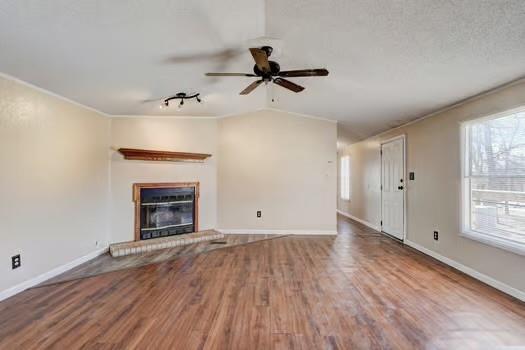 unfurnished living room featuring wood finished floors, baseboards, lofted ceiling, crown molding, and a brick fireplace