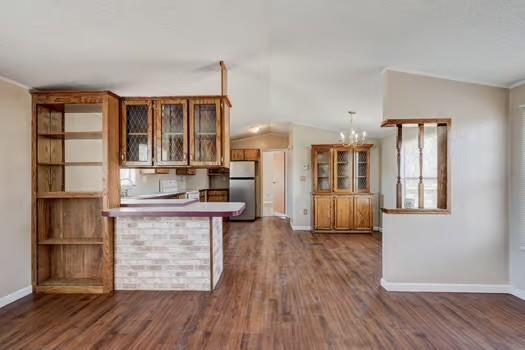 kitchen with lofted ceiling, freestanding refrigerator, dark wood-type flooring, glass insert cabinets, and brown cabinets