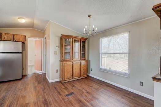 unfurnished dining area with baseboards, lofted ceiling, wood finished floors, and crown molding