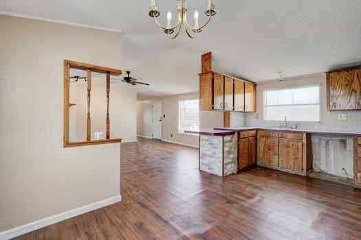 kitchen with brown cabinetry, baseboards, a sink, dark wood-type flooring, and ceiling fan with notable chandelier