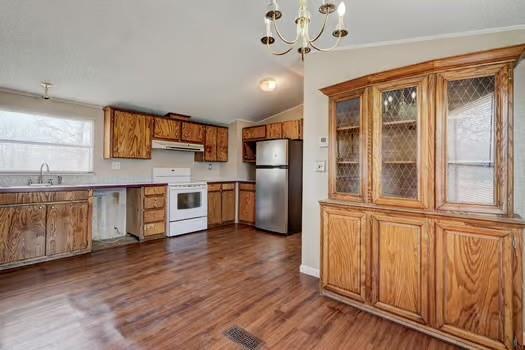 kitchen featuring under cabinet range hood, lofted ceiling, freestanding refrigerator, white electric range oven, and a sink