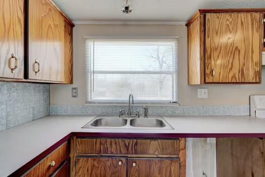 kitchen with light countertops, ornamental molding, brown cabinetry, and a sink