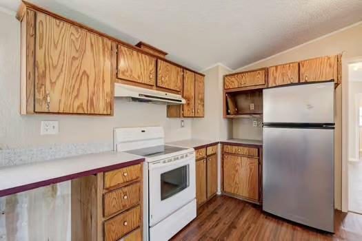 kitchen with under cabinet range hood, light countertops, lofted ceiling, freestanding refrigerator, and electric range