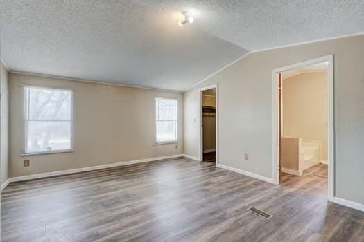 unfurnished bedroom with a textured ceiling, wood finished floors, and vaulted ceiling