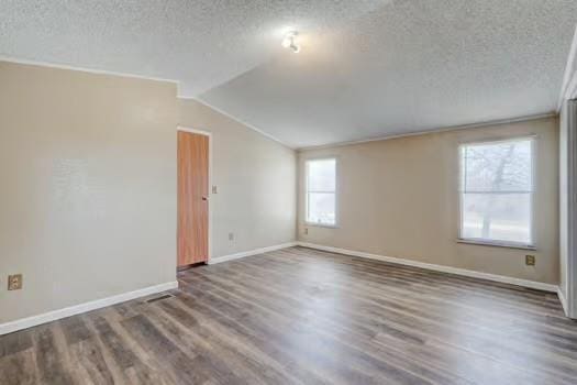 empty room with a textured ceiling, vaulted ceiling with beams, and wood finished floors