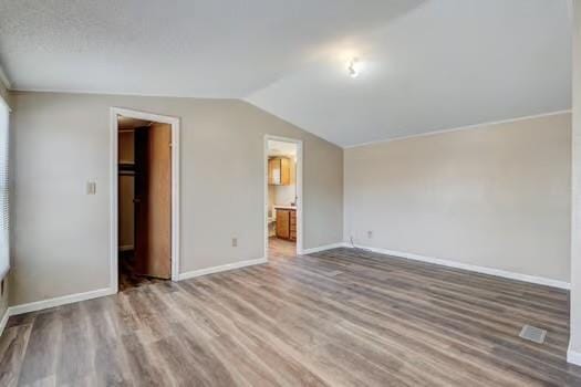 unfurnished bedroom with a spacious closet, connected bathroom, baseboards, lofted ceiling, and wood finished floors