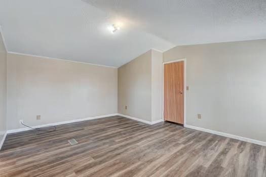 empty room with baseboards, lofted ceiling, and wood finished floors