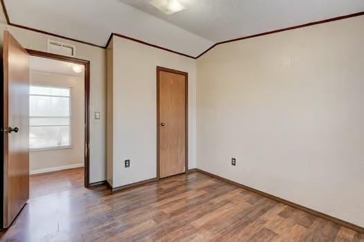 unfurnished bedroom featuring crown molding, baseboards, vaulted ceiling, wood finished floors, and a closet