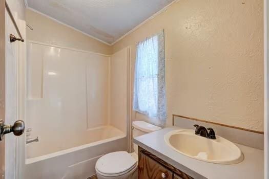 bathroom featuring toilet, crown molding, lofted ceiling, vanity, and a textured wall