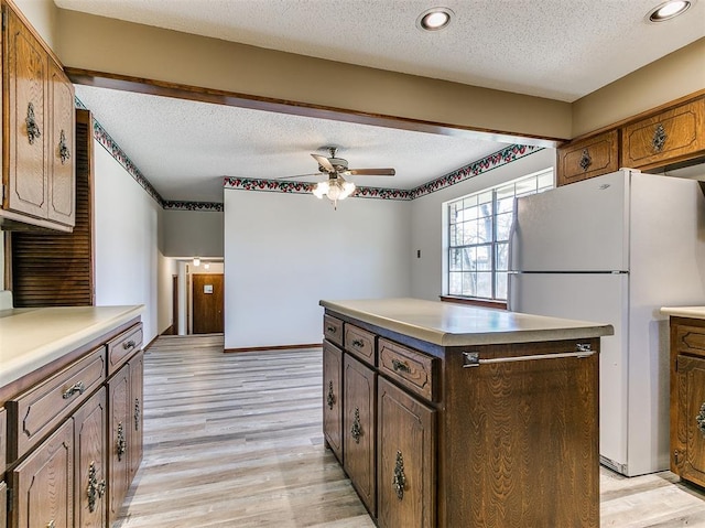 2000 N Alexander Ln, Bethany, OK 73008 - kitchen with freestanding refrigerator, a textured ceiling, light wood-type flooring, a center island, and a ceiling fan