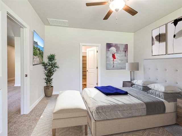 carpeted bedroom with a walk in closet, visible vents, ceiling fan, and baseboards