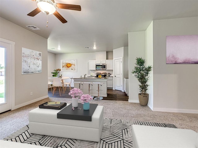 living room featuring a ceiling fan, dark carpet, visible vents, and baseboards