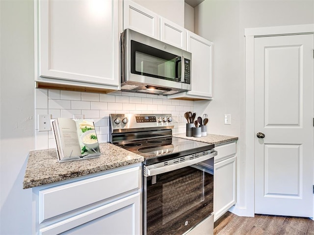 kitchen with stainless steel appliances, backsplash, white cabinetry, light stone countertops, and light wood-type flooring