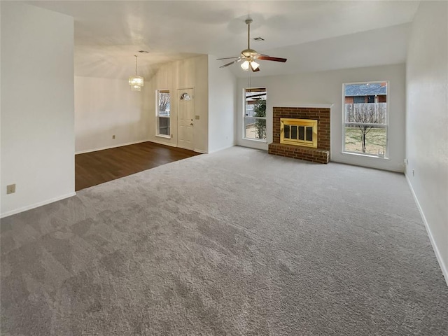 unfurnished living room with baseboards, carpet floors, lofted ceiling, a brick fireplace, and ceiling fan with notable chandelier