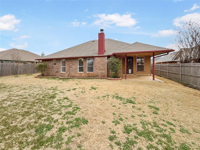 back of property featuring a fenced backyard, a yard, brick siding, a chimney, and a patio area