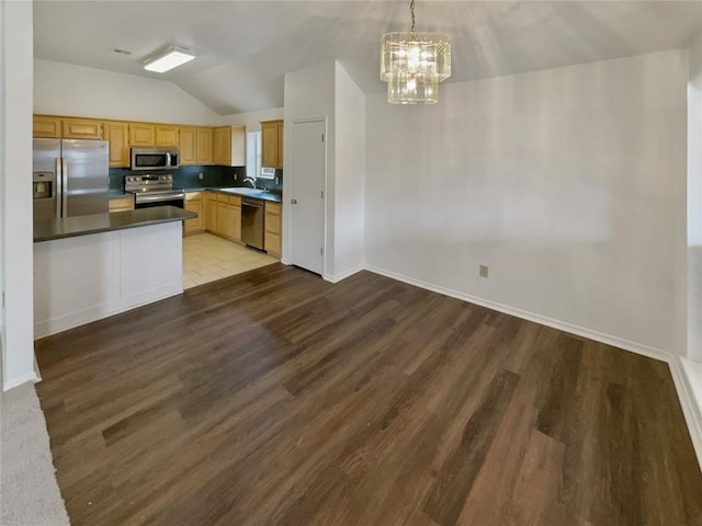 kitchen featuring a sink, dark countertops, wood finished floors, stainless steel appliances, and lofted ceiling