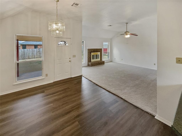 foyer entrance featuring visible vents, ceiling fan with notable chandelier, wood finished floors, baseboards, and a brick fireplace