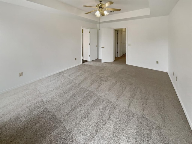 carpeted empty room featuring a raised ceiling, a ceiling fan, and baseboards