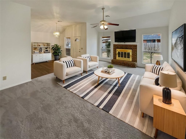 living area featuring a brick fireplace, a healthy amount of sunlight, carpet flooring, and ceiling fan with notable chandelier