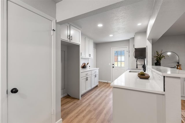 kitchen with light wood finished floors, white cabinetry, light countertops, and a sink