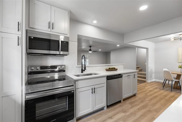 kitchen featuring a ceiling fan, a sink, light wood-style floors, appliances with stainless steel finishes, and tasteful backsplash