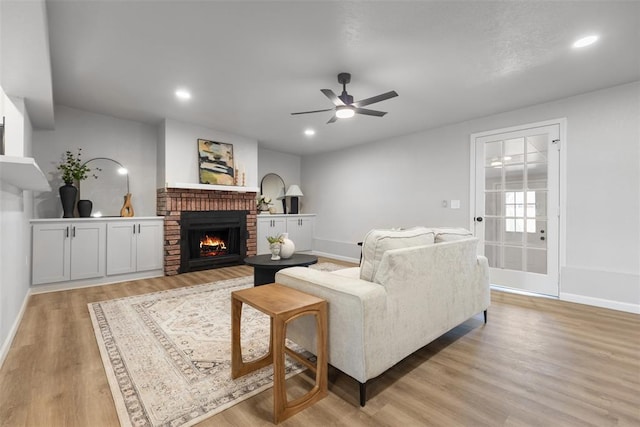 living area featuring baseboards, light wood-style floors, a brick fireplace, and a ceiling fan