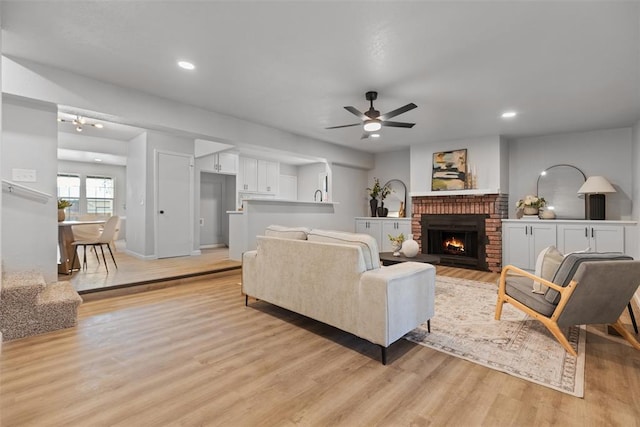 living room featuring a brick fireplace, light wood-style flooring, recessed lighting, and a ceiling fan