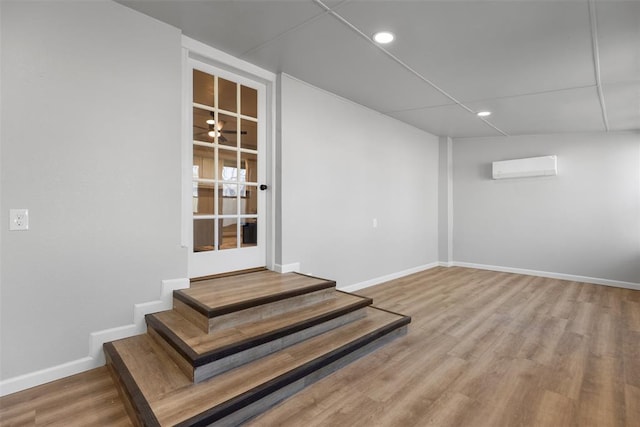 below grade area featuring stairway, wood finished floors, baseboards, and a wall mounted AC