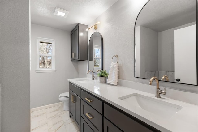 bathroom with marble finish floor, a textured ceiling, toilet, and a sink