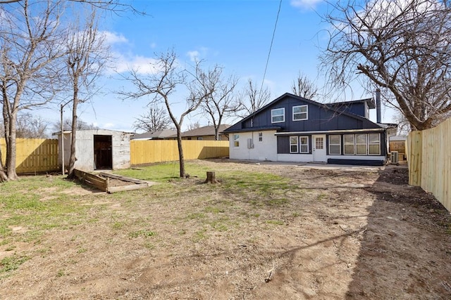 back of house featuring a lawn, a fenced backyard, a shed, an outdoor structure, and a sunroom