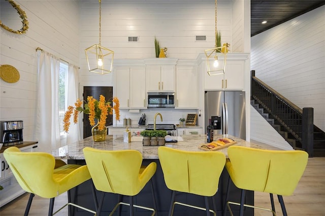 kitchen with stainless steel appliances, visible vents, a kitchen island with sink, and white cabinets