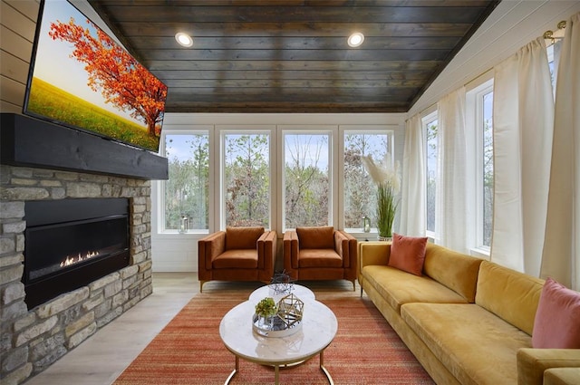 living area featuring wood finished floors, lofted ceiling, a stone fireplace, and wooden ceiling